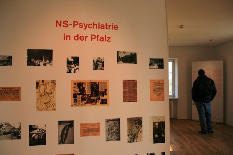 Das Bild zeigt zwei Rollups der Ausstellung NS-Psychiatrie in der Pfalz mit historischen Fotos. Ein Besucher schaut sich die Ausstellung an.