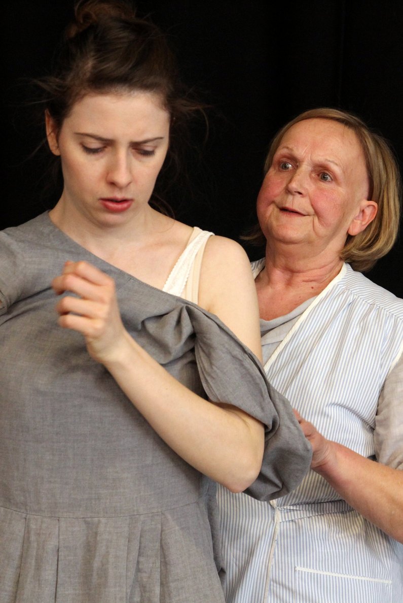 Eine ältere Frau steht hinter einer jüngeren Frau und hält sie am Arm- Szene aus dem Theaterstück "Rosa B. - beinahe vergessen"